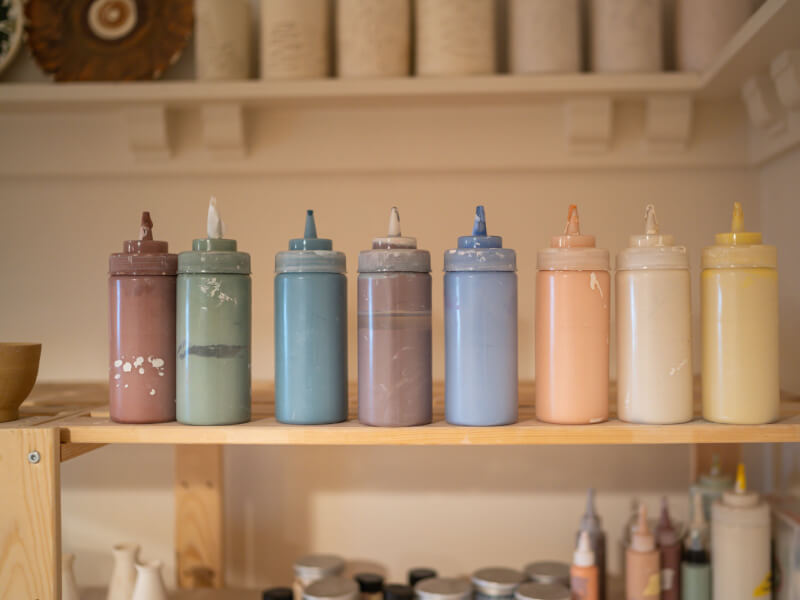 A line up of paint bottles on a shelf in a pottery studio.